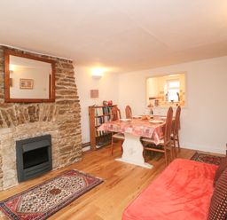 A dining area with table and chairs next to a stone fireplace and a red sofa at River Cottage in Burton Bradstock