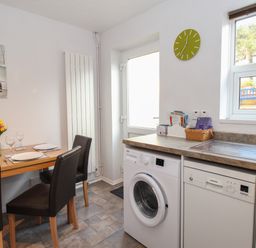 A kitchen with a dining table set with plates and glasses a washing machine dishwasher sink window and door at Rockpools in Weymouth