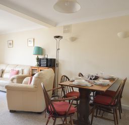 A living room with a dining table set for four and beige sofas with cushions at Sanjernin Swanage
