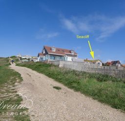 A dirt path leading uphill with grass on both sides and houses with fences on the right side at Seacliff West Bay
