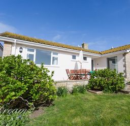A single story house with a patio table and chairs in a garden at Seacliff in West Bay