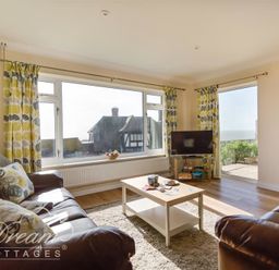 A living room with two leather sofas a coffee table a television and large windows showing houses and a garden at Seacliff in West Bay