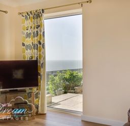 A corner of a room with a television on a glass stand and a large window showing a view of the sea at Seacliff in West Bay