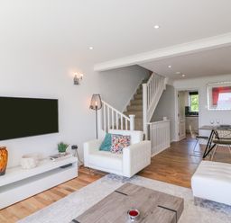 A living room with a mounted TV white chair and dining table near stairs at Sea King House in Cove Castle