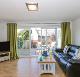 A living room with a black leather sofa and green curtains overlooking a patio at Sea Pebbles in Weymouth
