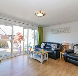 A living room with black leather sofas and a coffee table next to sliding glass doors at Sea Pebbles in Weymouth