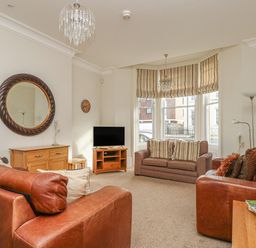 A living room with two brown leather sofas a brown fabric loveseat a wooden cabinet a round mirror and a television at Sea Star in Weymouth