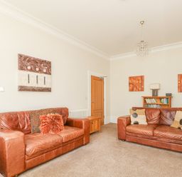 A living room with two brown leather sofas cushions a bookshelf and artworks on the walls at Sea Star in Weymouth
