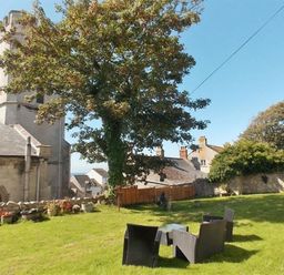 An outdoor garden area with chairs and a table near a large tree and stone building at St Johns View Portland