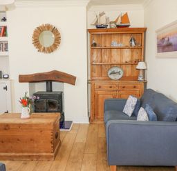 A living room with a blue sofa wooden coffee table and woodburner at Studland Cottage in Studland
