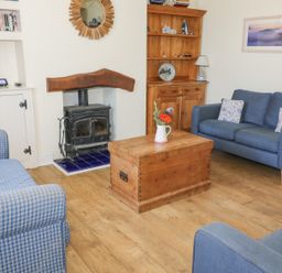A living room with a wood stove a wooden chest as a coffee table two blue sofas a wooden cabinet and a bookshelf at Studland Cottage in Studland