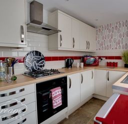 A kitchen with white cabinets red microwave and kettle a gas stove and patterned wallpaper at Sunny Days in Weymouth