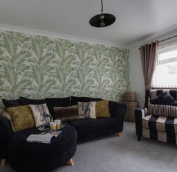 A living room with a black sofa and cushions next to a striped armchair with cushions and a large window at Sunny Days in Weymouth