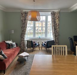 A living room with a red sofa two black armchairs a wooden dining table and a large window with floral curtains at Tradewinds Brewers Quay Harbour