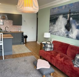A living room with a red sofa and pillows next to a kitchen area with gray cabinets at Tradewinds Brewers Quay Harbour