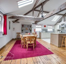 A dining area with wooden table and chairs on a red rug next to a kitchen with stools and white cabinets at Upsidedown House in Brewers Quay Harbour