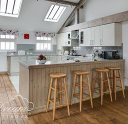 A kitchen with wooden stools at a counter and white cabinets at Upsidedown House in Brewers Quay Harbour