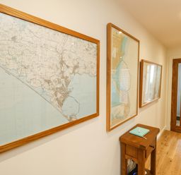A hallway with framed maps on the wall a wooden table with a book and a wooden door at Waters Edge in Wyke Regis