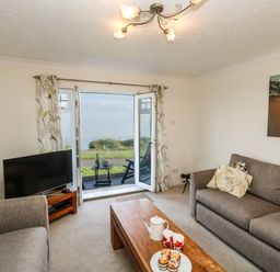 A living room with two sofas a wooden coffee table a TV and an open door leading to a balcony overlooking the sea at Waters Edge in Wyke Regis