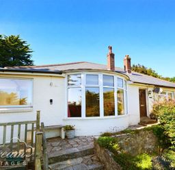 A white single-story house with a curved window and two chimneys surrounded by greenery at Waterson in Osmington