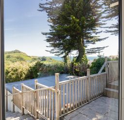A view through a window of a wooden deck and railing with trees and hills in the background at Waterson in Osmington