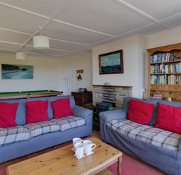 A living room with two sofas with red cushions a wooden coffee table with mugs a bookshelf and a fireplace at Waterson in Osmington