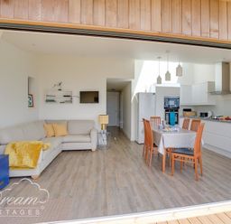 An open living space with a sofa, dining table, chairs, and kitchen appliances at The Wave in Eype