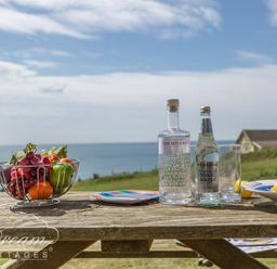 A wooden picnic table with a bowl of fruit plates bottles and glasses by the sea at The Wave in Eype