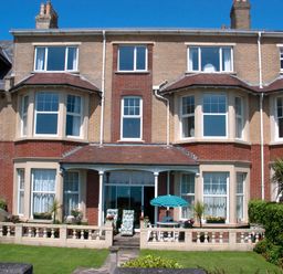 A view of a brick house with bay windows a small porch and a garden with outdoor furniture at Weymouth Bay Apartment B in Greenhill