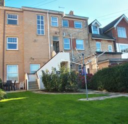 A backyard with a green lawn and bushes and a clothesline next to a brick apartment building Weymouth Bay Apartment B Greenhill