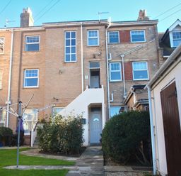 A backyard garden with green grass bushes a clothesline and brick houses at Weymouth Bay Apartment B in Greenhill
