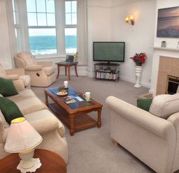 A living room with beige sofas green cushions a wooden coffee table a television and a window showing the sea at Weymouth Bay Apartment B in Greenhill
