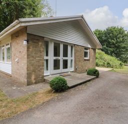 An exterior view of a single story brick house with white framed doors and windows and surrounding trees at Woodlands Cottage in Ringstead