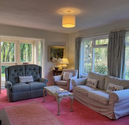 A sitting room with two sofas armchair coffee table lamp and windows at Woodlands Cottage in Ringstead