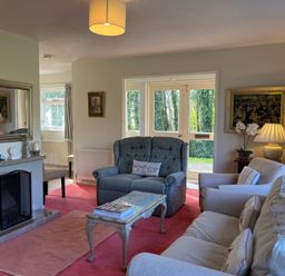 A living room with a fireplace armchairs a sofa a coffee table and a lamp at Woodlands Cottage in Ringstead