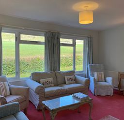 A living room with multiple armchairs and a sofa around a glass coffee table at Woodlands Cottage in Ringstead