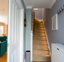 A hallway with carpeted stairs lit by small lights and a glimpse of a living room with a teal sofa at 16 Courtenay Street Salcombe