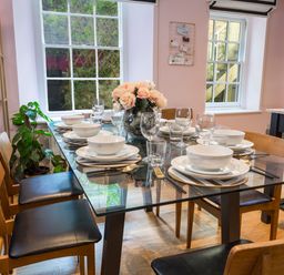 A dining room with a glass table set with plates bowls glasses and chopsticks with wooden chairs around the table at 16 Courtenay Street in Salcombe