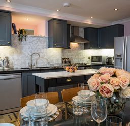 A kitchen with dark cabinets a marble island and a dining table with a flower vase at 16 Courtenay Street Salcombe