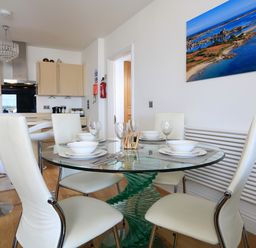 A kitchen and dining area with a glass round table and white chairs at 1 At The Beach in Torcross