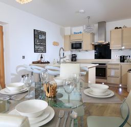 A kitchen with a glass dining table set with bowls and glasses at 1 At The Beach in Torcross