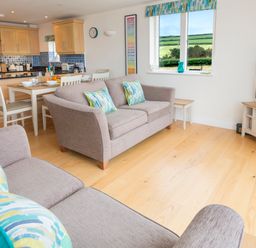 An open-plan living room and kitchen with sofas, dining table, kitchen cabinets, and a television at 2 Ocean's Edge in Thurlestone