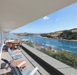 A balcony with wooden chairs and table overlooking a river with boats and hills in the background at 2 Poundstone Court in Salcombe