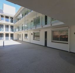 An open courtyard of a multi level building with glass railings and several doors and windows at 2 Poundstone Court in Salcombe