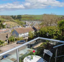 A balcony with a white table and chair overlooking a residential area with houses hills and a marina at 2 Rockmount in Salcombe