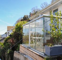 A balcony with glass railing and white chairs and table next to plants at 2 Rockmount in Salcombe