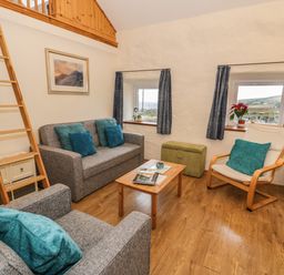 A living room with grey sofas and blue cushions a wooden coffee table and a white armchair at Y Bwthyn Elidir Fach Mountain near Llanberis
