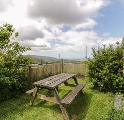A wooden picnic table on grass next to bushes and a white stone wall at Y Bwthyn in Elidir Fach Mountain near Llanberis