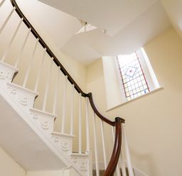 A staircase with white balusters and a dark wooden handrail near a window with stained glass at 3 Dartview in Dartmouth