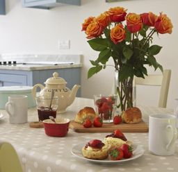 A kitchen table with a teapot jam scones strawberries mugs and a vase of roses at 3 Eddystone Row in Salcombe